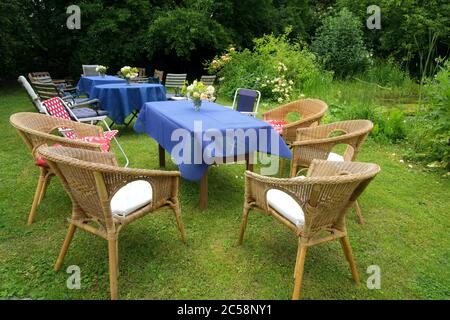 Richten Sie sich für eine lässige Sommerparty mit Tischen, blauen Tischdecken und vielen verschiedenen Stühlen in einem ländlichen Garten, ausgewählte Fokus Stockfoto