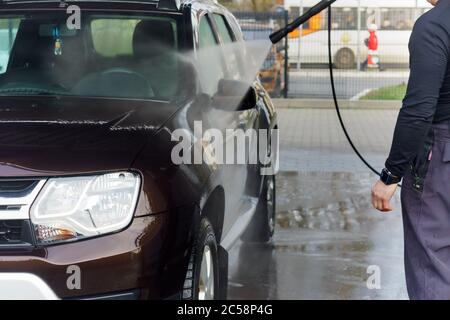 Ein Mann wäscht ein Auto bei einer berührungslosen Autowäsche, ein Mann wäscht ein braunes Auto, Kaliningrad, Russland, 1. März 2020 Stockfoto