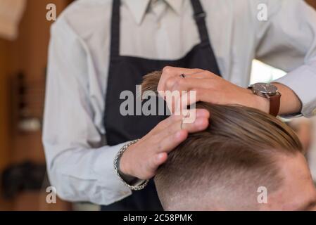 Professionelle Hände von Friseur Master Styling Haar für Kunden Friseurladen, junger Kerl. Haarpflege, sammelt Haare in einem Pferdeschwanz, professionelle Haare Stockfoto