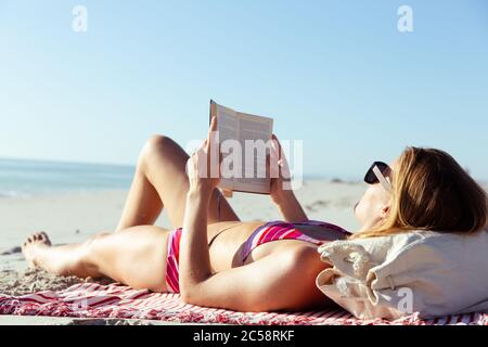 Frau liest ein Buch, während sie am Strand liegt Stockfoto