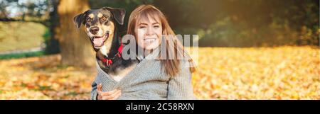 Glückliche junge kaukasische Frau umarmenden Hund. Besitzer zu Fuß mit Haustier am Herbst Tag. Beste Freunde, die Spaß im Freien haben. Freundschaft des Menschen mit häuslichen Stockfoto