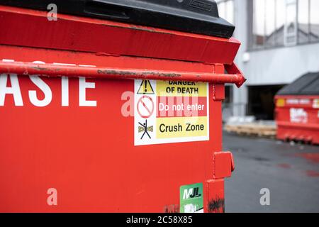 Überfließender Industrieabfallbehälter, voll mit gebrauchten Kunststoffbeuteln. Der Behälter befindet sich in einem Industriekomplex mit alten Gebäuden im Mühlenstil. Stockfoto