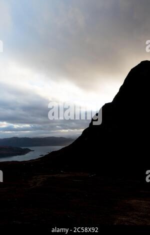 Silhouette von Bealach na Ba Berg mit dramatischen Sonnenuntergang und Sturmwolken, Blick auf Loch Carron Küste und Berge dahinter, Highlands of Scotland Stockfoto