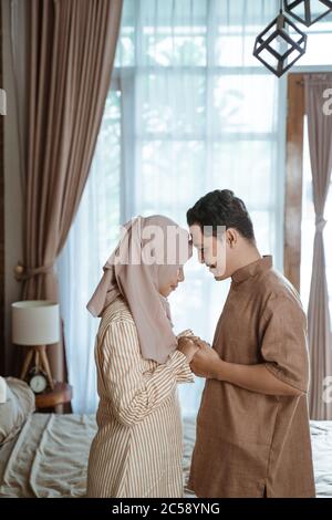 Junge muslimische Paar lächelt sich gegenseitig auf die Stirn und hält die Hände, während sie im Zimmer stehen Stockfoto