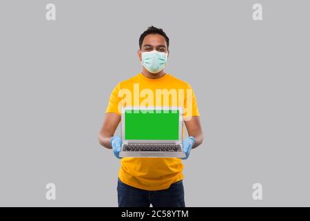 Lieferung Mann zeigt Laptop Green Screen Tragen von medizinischen Maske und Handschuhe. Home-Bestellungen, Quarantäne-Lieferung, Online-Shopping, Freiberufler-Konzept. Stockfoto