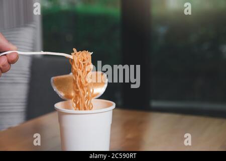 Hand eines Mannes, der eine Kunststoffgabel mit gekochten Instant-Nudeln hält. Eine Tasse Instant Nudel mit Gabel bereit zu essen bequeme und leckere Speisen. Stockfoto