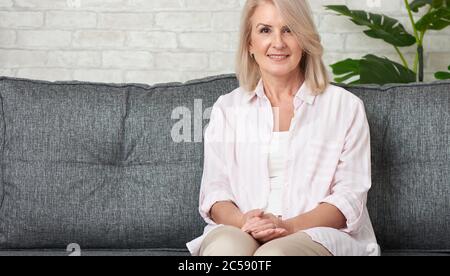 Schöne 50-jährige Frau, die sich auf dem Sofa entspannt Stockfoto