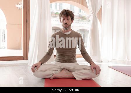 Yogalehrer sitzt in der Lotusposition mit geschlossenen Augen. Mann praktiziert Yoga. Wie man die Arme für eine Kriya oder Meditation hält. Stockfoto