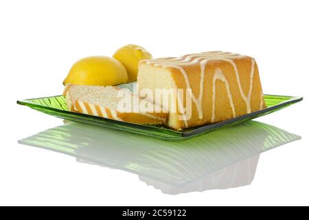 Zitronenkuchen und zwei Scheiben auf grünem Glasplatte, Zitronen im Hintergrund, isoliert auf weißem Hintergrund Stockfoto