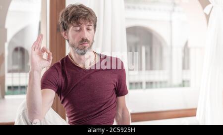 Portrait des bärtigen Mannes, der Yoga in Matsyendrasana Pose - herr der Fische Pose. Wie man die Arme in der Luft hält für eine Kriya oder Meditation. Stockfoto