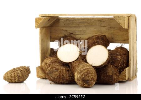 Ein Bündel Tarowurzel (Colocasia) in einer Holzkiste auf weißem Hintergrund Stockfoto