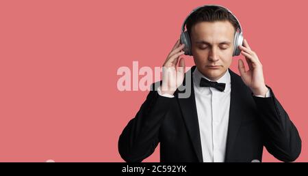 Modischer, schöner Mann mit Kopfhörern, der Musik hört. Isoliert auf rosa Hintergrund Stockfoto