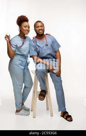 Schönes Paar junger afroamerikanischer Ärzte mit Stethoskopen, die isoliert auf weißem Studiorgrund lächeln. Copyspace. Konzept der Gesundheitsversorgung und Medizin, Pflege, Behandlung, Diagnostik. Stockfoto