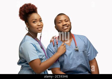 Schönes Paar junger afroamerikanischer Ärzte mit Stethoskopen, die isoliert auf weißem Studiorgrund lächeln. Copyspace. Konzept der Gesundheitsversorgung und Medizin, Pflege, Behandlung, Diagnostik. Stockfoto