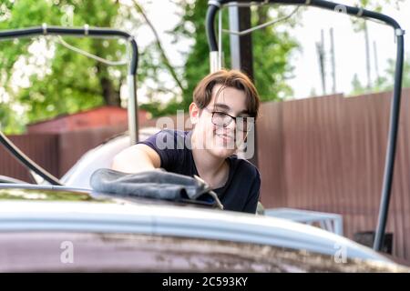 Junger Mann in Brille wäscht sein Auto und lächelt Stockfoto