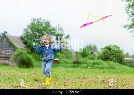 Kleines Mädchen 3-5 Jahre alt in Jeans, Jacke und Gummistiefel startet einen Drachen Stockfoto