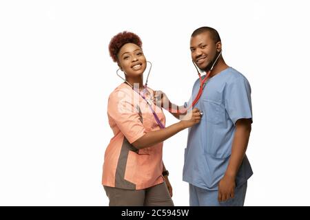 Schönes Paar junger afroamerikanischer Ärzte mit Stethoskopen, die isoliert auf weißem Studiorgrund lächeln. Copyspace. Konzept der Gesundheitsversorgung und Medizin, Pflege, Behandlung, Diagnostik. Stockfoto