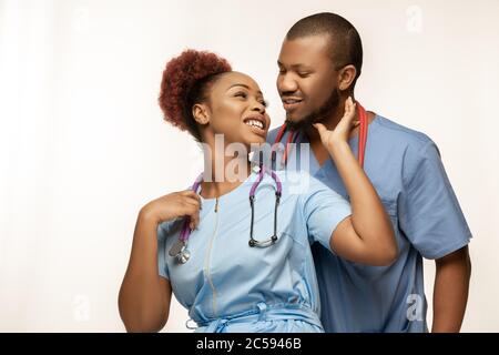 Schönes Paar junger afroamerikanischer Ärzte mit Stethoskopen, die isoliert auf weißem Studiorgrund lächeln. Copyspace. Konzept der Gesundheitsversorgung und Medizin, Pflege, Behandlung, Diagnostik. Stockfoto