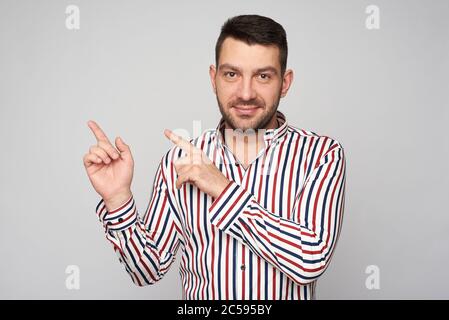 Der gutaussehende bärtige Mann zeigt mit den Fingern den Raum zu kopieren. Isoliert auf Grau Stockfoto