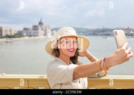 Glückliche junge Frau, die Selfie auf der Margaretenbrücke, Budapest, Ungarn macht Stockfoto