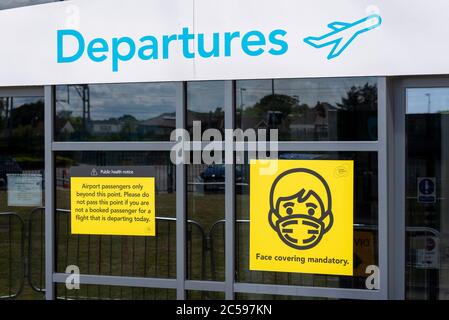 Hinweisschilder mit Gesichtsbedeckung am Flughafen London Southend, Essex, Großbritannien, nach der COVID-19 Coronavirus-Sperre. Eingang für Abfahrten. Flüge wieder aufgenommen Stockfoto