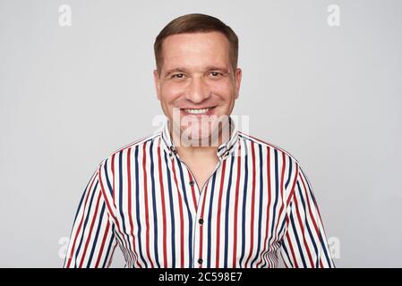 Fröhlicher Mann mittleren Alters ist lächelnd trägt gestreiftes Hemd isoliert auf grau Stockfoto