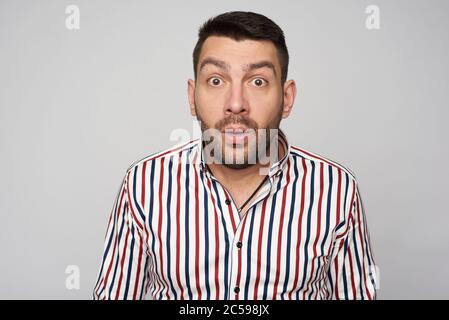 Überrascht bärtig schöner Mann trägt gestreiftes Hemd. Isoliert auf grauem Hintergrund Stockfoto