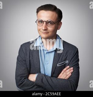 Positiver junger Mann mit Jacke und Brille lächelnd. Isoliert auf grauem Hintergrund Stockfoto