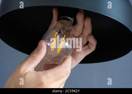 Nahaufnahme. Eine Hand wechselt eine Glühbirne in einer stilvollen Loft-Lampe. Spirallampe aus Filament. Moderne Innenausstattung Stockfoto