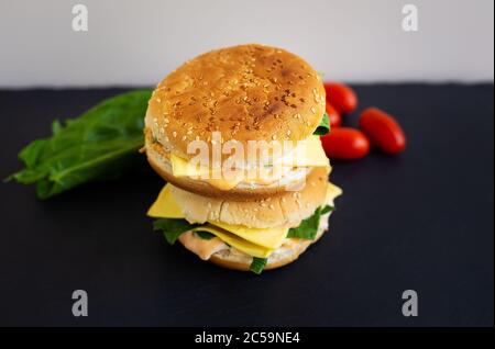 Leckerer Hamburger mit Tomaten, Cutlet, Brunnenkresse und Zwiebeln auf schwarzem Schiefer, im Hintergrund Salat und Kirschtomaten. Leerzeichen für Text Stockfoto