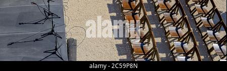 Panoramabild einer Bühne mit Mikrofonen und Reihen von braunen Holzstühlen im Freien Stockfoto