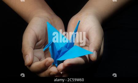Hand halten Origami Papier Kran Blue Bird. Auf schwarzem Hintergrund Stockfoto