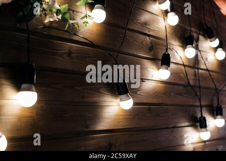 Einrichtung mit leuchtenden Lampen und Blumen an einer Holzwand Hintergrund in der Nähe Stockfoto