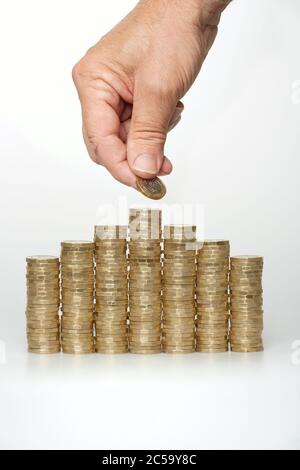 Foto einer Hand eines Mannes, der eine £1-Münze auf Stapel neuer uk £1-Münzen legt (Münzen im Umlauf nach Oktober 2017). Die Münzen bilden eine Hausform. Stockfoto