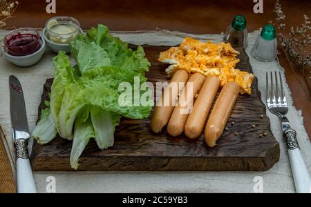 Kontinentales Frühstück mit Rührei, Bratwürsten, Gemüse und Scones auf Holzhintergrund, selektiver Schwerpunkt. Stockfoto