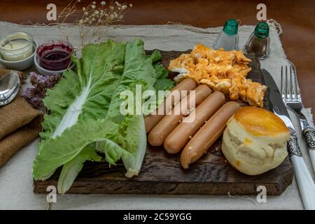 Kontinentales Frühstück mit Rührei, Bratwürsten, Gemüse und Scones auf Holzhintergrund, selektiver Schwerpunkt. Stockfoto