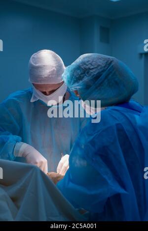 Kinderchirurgen führen urologische Operationen durch. Ein Mann und eine Frau in einer Maske und einem blauen sterilen Gewand im Operationssaal. Stockfoto