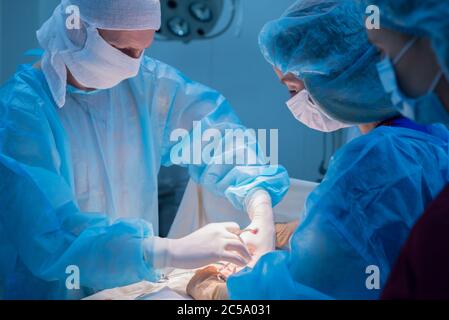 Kinderchirurgen führen urologische Operationen durch. Ein Mann und eine Frau in einer Maske und einem blauen sterilen Gewand im Operationssaal. Stockfoto