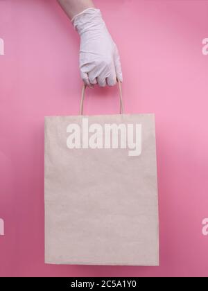 Frau, die Papiertüte hält, Hand in medizinischen Handschuh als Schutz vor Viren. Kontaktlose Lieferung während der Quarantänezeit. Stockfoto