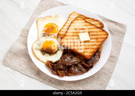 Hausgemachte gesunde Sunnyside Eier Frühstück auf einem weißen Teller auf einem weißen Holztisch, Seitenansicht. Stockfoto