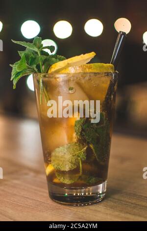 Kaltes Getränk mit Eiswürfeln, Zitronenscheiben, Minzblättern und einem schwarzen Stroh Stockfoto