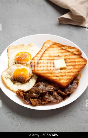 Hausgemachte gesunde Sunnyside Eier Frühstück auf einem weißen Teller auf einer grauen Oberfläche, Seitenansicht. Stockfoto