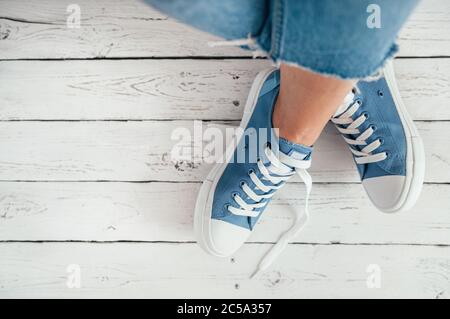 Teenager Füße in lässigen blauen neuen Sneakers auf dem weißen Holzboden Nahaufnahme Bild. Vintage-Stil in der modernen Modewelt Konzept Bild. Stockfoto