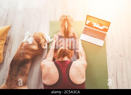 Draufsicht auf fit sportlich gesunde Frau sitzen auf Matte in Paschimottanasana Pose, tun Atemübungen, beobachten Online-Yoga-Kurs auf Laptop-Computer. H Stockfoto