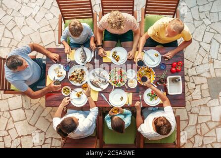 Großes Familienessen mit mehreren Generationen im Prozess. Tisch mit Essen und Händen. Nahrungsaufnahme und Familie mit mehreren Generationen Bild von oben Konzept Bild Stockfoto