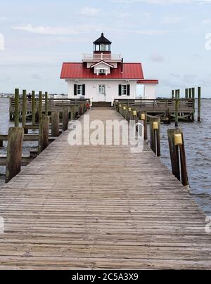 Ein kleiner Leuchtturm am Ende eines Piers mit rotem Dach und weißem Seitendach. Ein paar leichte Wolken ziehen den hellblauen Himmel. Stockfoto
