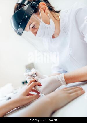 Maniküre Master in transparent Safety Face Shield mit elektrischen Nail Polisher Tool für die Verglasung Behandlung Maniküre Professionelle Verfahren. Kleiner Bus Stockfoto