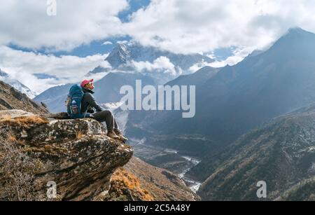 Junge Wandererin Backpacker sitzt am Klippenrand und genießt Ama Dablam 6,812m Gipfelblick während der Everest Base Camp (EBC) Trekking Route in der Nähe von Ph Stockfoto