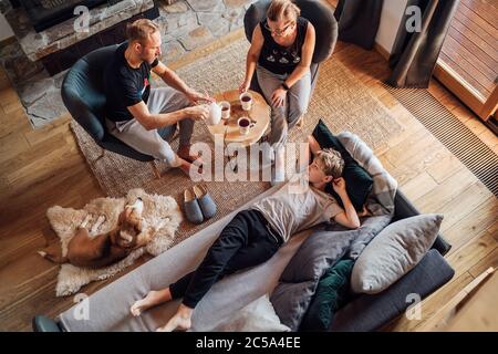 Friedliche Momente der Familie Konzept Bild. Gemütliche Familie trinkt Tee Zeit. Vater, Mutter und Sohn im Wohnzimmer. Junge liegt in bequemen Sofa und Stockfoto