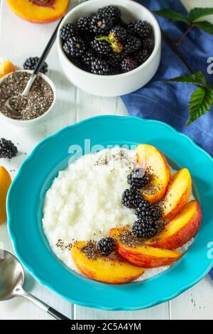 Gesunde Ernährung für Frühstück, Diät-Food-Konzept. Reisbrei mit Chia, Pfirsich und Brombeere in einer Schüssel auf einem weißen Holztisch. Stockfoto